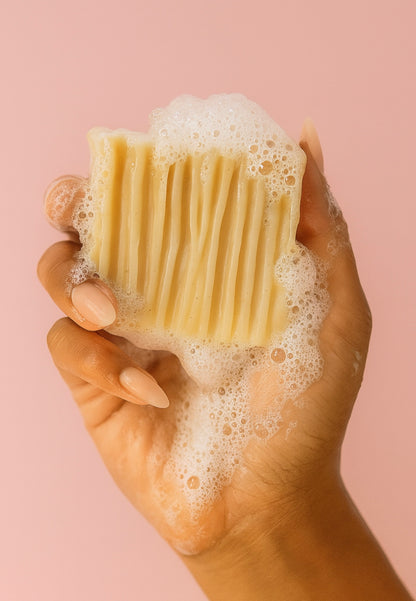 Artisan oatmeal soap with textured ridges, foaming in use, photographed in a woman’s hand against a pastel pink backgrou