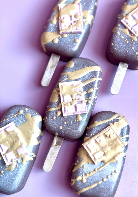 Birthday cake–inspired luxury popsicle soaps featuring shimmering brown bases, golden drizzle, and confection-style topping by Decadent Body Bar.
