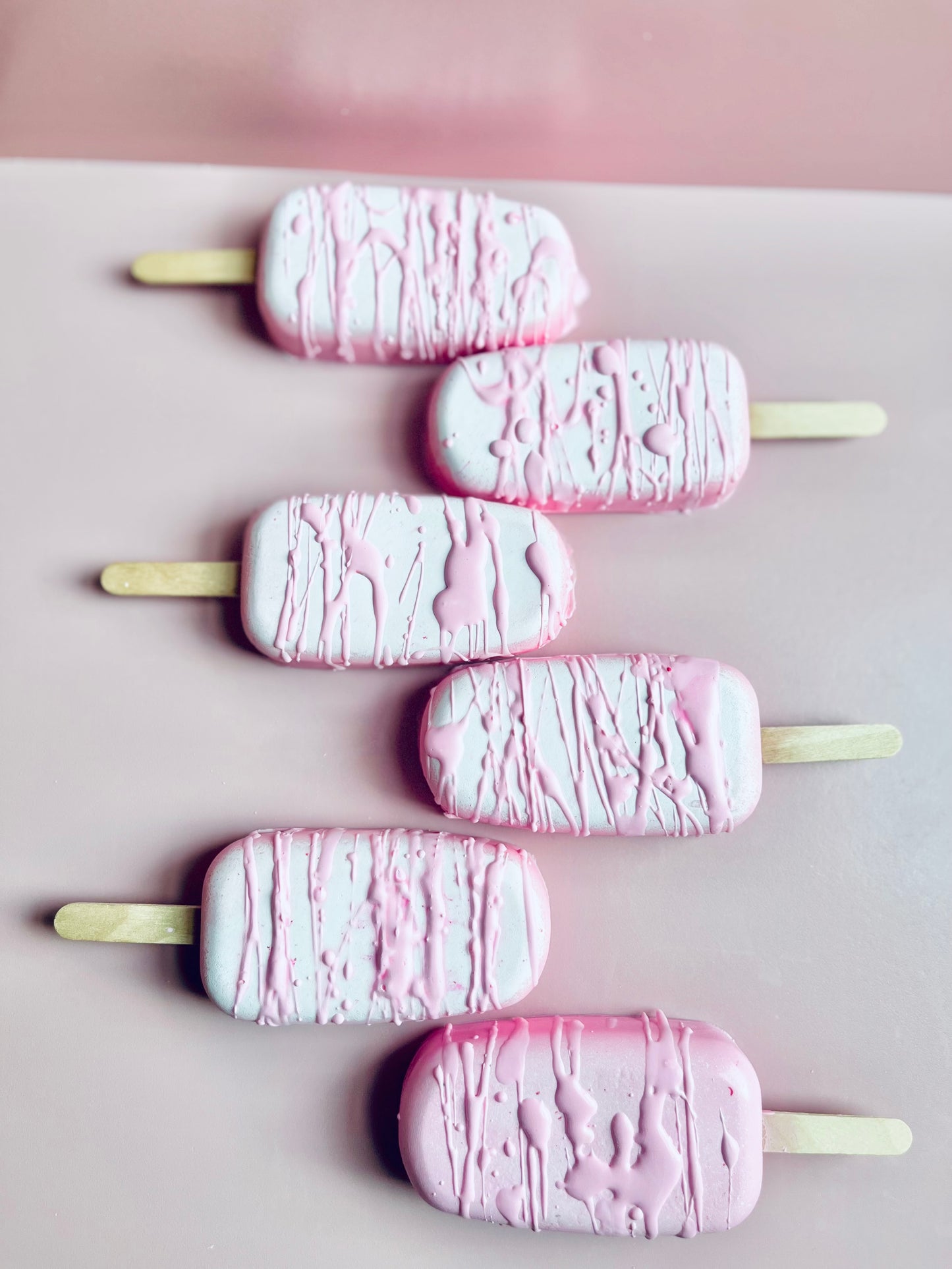 Decadent Body Bar dessert-style artisan soap shaped like a popsicle in pastel pink and white with drizzle finish on a blush pink background.