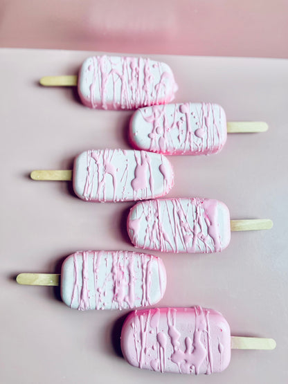 Decadent Body Bar dessert-style artisan soap shaped like a popsicle in pastel pink and white with drizzle finish on a blush pink background.