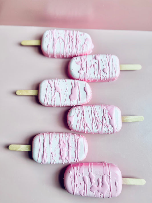 Decadent Body Bar dessert-style artisan soap shaped like a popsicle in pastel pink and white with drizzle finish on a blush pink background.